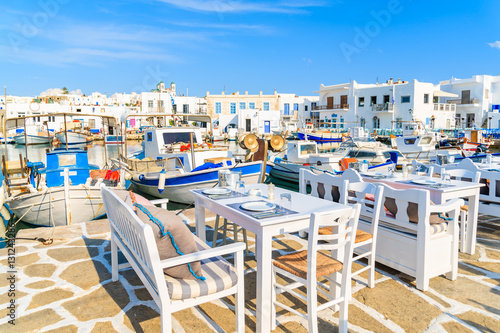 Greek taverna tables and fishing boats anchoring in Naoussa port, Paros island, Greece