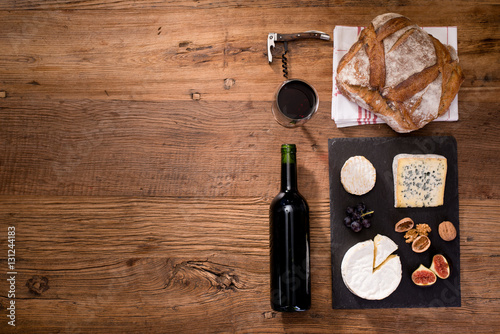 above overhead view flat lay assortment of various cheese with traditionnal bread fruits glass and bottle of red wine on old wooden table