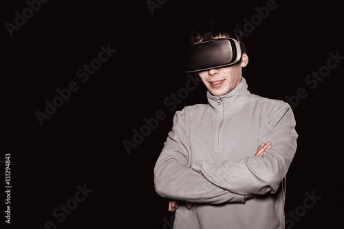 A young man wearing virtual reality glasses to watch movies or play video games. It is isolated on a black background. Design headset is of a general nature and is not logos.