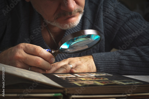 Man considers album of postage stamps trough the magnifying glass horizontal