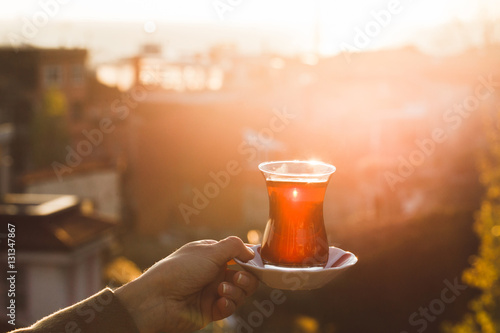 Hand holding a cup of traditional Turkish tea illuminated and tr