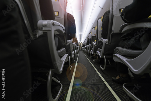 Inside the airplane : Modern interior of aircraft. Black seats inside airplane with flare light. Symmetric vanishing row of seats inside air transport. Economy class of flight.