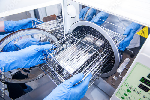 Dentist assistant's hands get out sterilizing medical instruments from autoclave. Selective focus