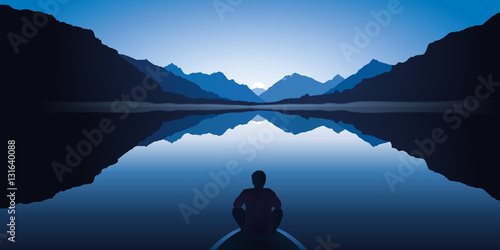 Un homme zen, assis à l’avant d’une barque, médite en contemplant le paysage calme et magnifique d’un lac entouré de montagnes.
