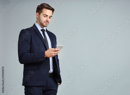 Handsome young businessman with phone on gray background