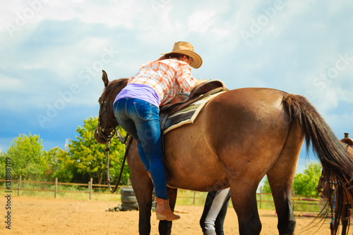 Cowgirl getting horse ready for ride on countryside