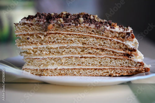 Кусок медового домашнего торта на белом блюдце на кухонном столе 
