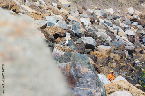 Man in Orange Fishing on Rocks - Stock Imge