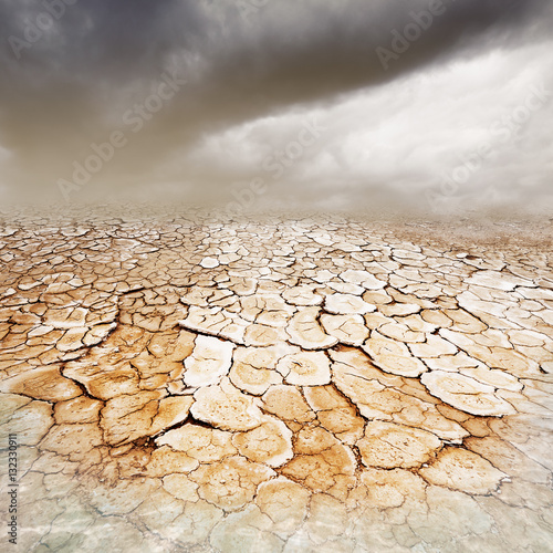 Dry, parched cracked earth with stormy dusty sky and foreground water
