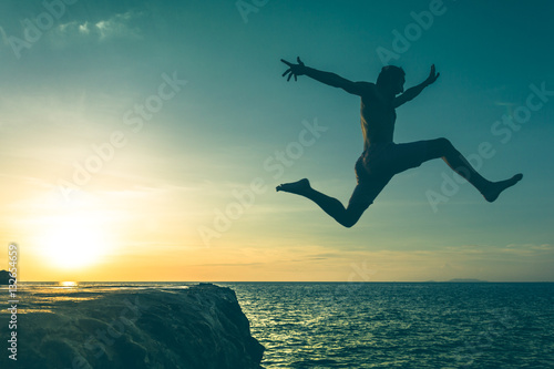 Fearless young man jumping over a cliff into the sea on sunset in Koh Phangan island, Thailand. Vintage effect.