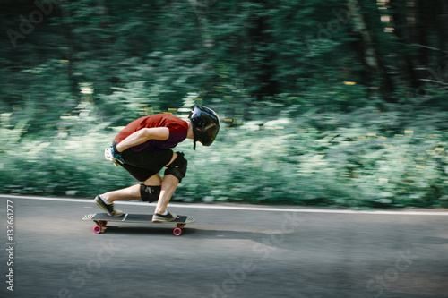 Skater boy in helmet on longboard going on road in beauty nature