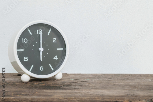 Closeup black and white alarm clock for decorate in 6 o'clock on old wood desk and white cement wall textured background with copy space
