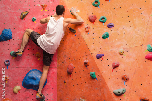 Man climber on artificial climbing wall in bouldering gym