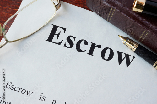 Paper with word Escrow and glasses on a table.