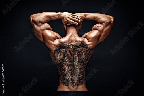 Unrecognizable muscular man with tattoo on back against of black background. Isolated.