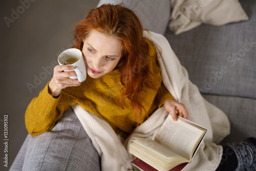 attraktive frau mit einer tasse kaffee und einem buch auf dem sofa