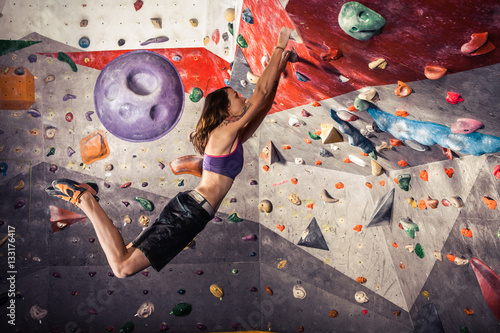 young woman climbing artificial boulder indoors