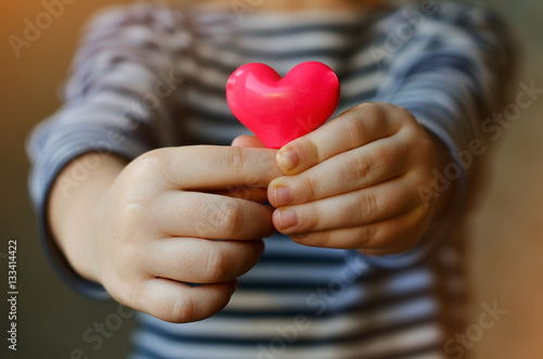 child holding a small pink heart. symbol of love, family, hope. Backgrounds for cards on Valentine's Day. Backgrounds for social posters about the preservation of the family and children.