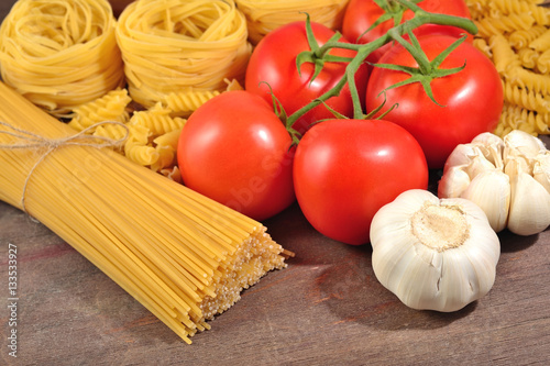 Uncooked Italian pasta, ripe tomatoes branch, and garlic