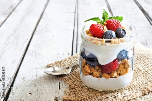 Healthy blueberry and raspberry parfait in a mason jar on a rustic white wood background
