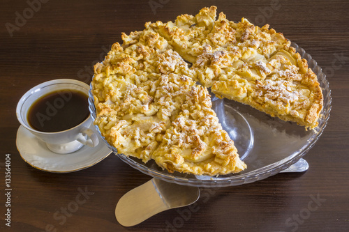 Apple charlotte in a large glass vase. With a cup of black coffee and a shovel for a cake. Still life. Polish cuisine..