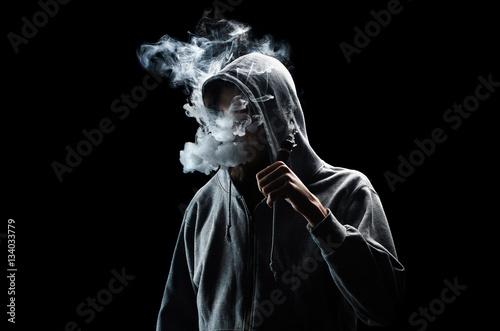 One man in the hood vaping e-cigarette and blowing a cloud.