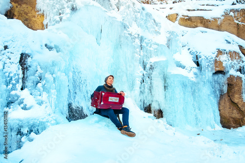 Happy young man playing the harmonium on a frozen waterfall