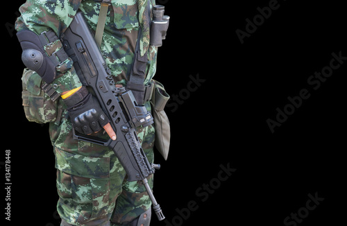 soldier in uniform holding automatic assault rifle on black background