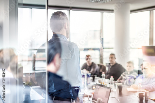 Business man making a presentation at office. Business executive delivering a presentation to his colleagues during meeting or in-house workshop. Rear view. Business and entrepreneurship.