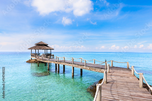 Tropical beach landscape with wooden pier above transparent sea