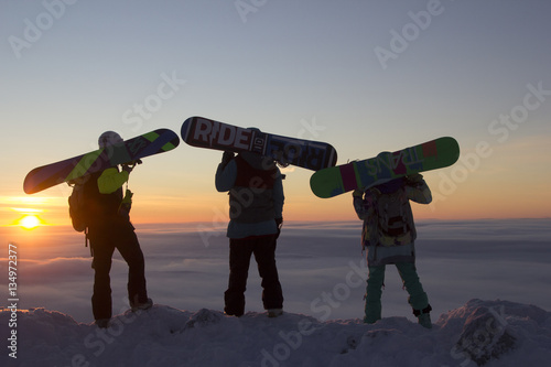 Three snowboarders standing on top of a mountain at dawn