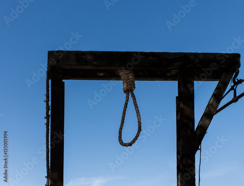 Wooden hangman's gallows with rope noose against blue sky