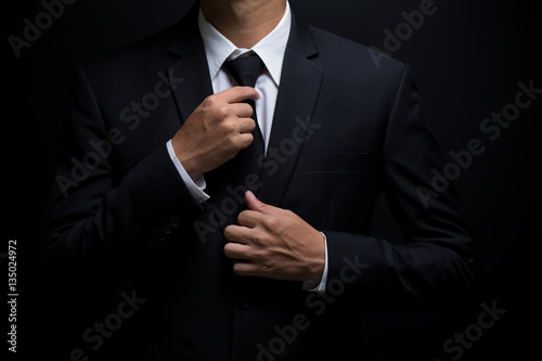 Man in black suit and adjusting his necktie