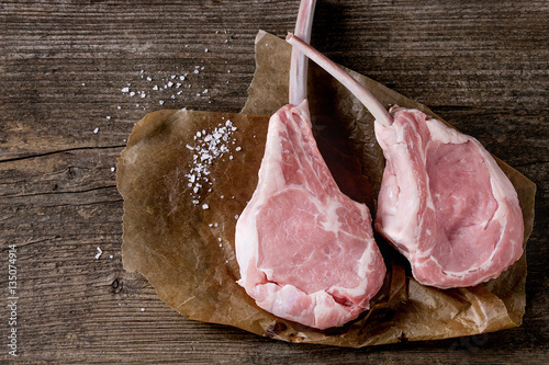 Two raw uncooked Veal tomahawk steak with sea salt on baking paper over old wooden background. Top view with space.
