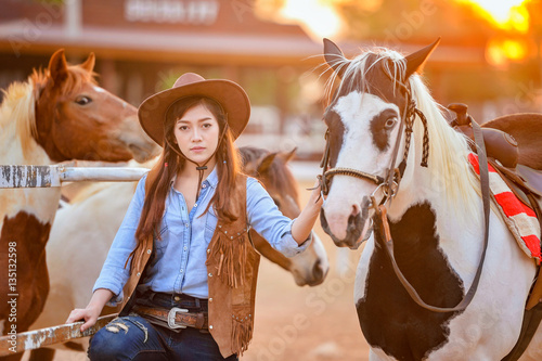 Beautiful womam sensuality elegance woman cowgirl on during sunset, riding a horse. Clothed blue jeans, brown leather jacket and hat. Has slim sport body. People and animals. Equestrian. vintage style