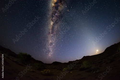 Starry sky and Milky Way arc, outstandingly bright, with rising moon, captured from the Namib desert in Namibia, Africa. The Small Magellanic Cloud on the left hand side.