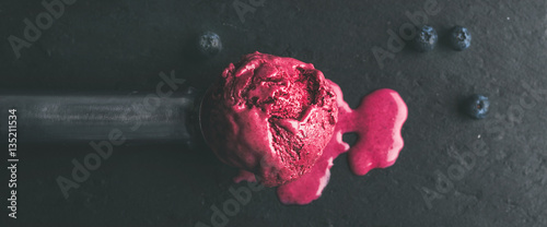 Melting scoop of blueberry ice-cream over black slate stone background, top view, selective focus