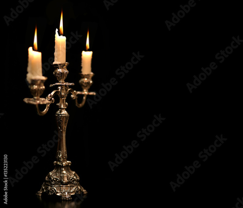 burning old candle vintage Silver bronze candlestick. Isolated Black Background.