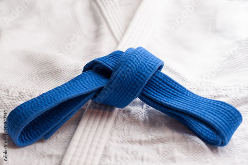 Blue judo, aikido or karate belt tied in a knot with white kimono in background