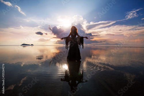 Elegant woman walking on water. Sunset and silhouette.