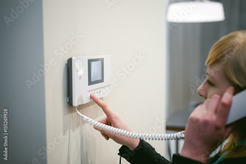 blonde woman hangs up the phone after answering the intercom call in her apartment