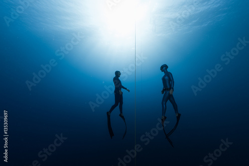 Two free divers, man and woman, ascending from the depth