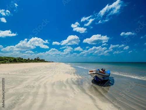 Isolated Boat on Amazing Beautiful scenic unspoiled white sand sandy beach with sand pattern and blue sky with white clouds near Pigeon Island in Trincomalee, Sri Lanka