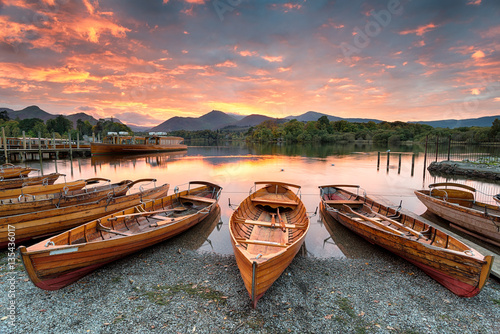 A fiery sunset over boats on the shore of Derwentwater at Keswick in the Lake District in Cumbria