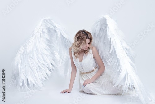 beautiful young model with big angel wings sitting in the studio. white background