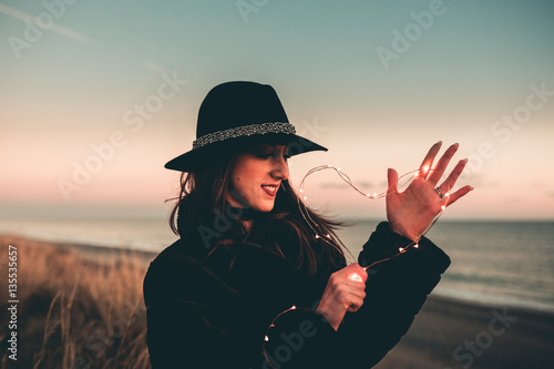 Cuore luminoso tenuto in mano da una ragazza vestita di nera sulla spiaggia al tramonto. San Valentino Concetto.