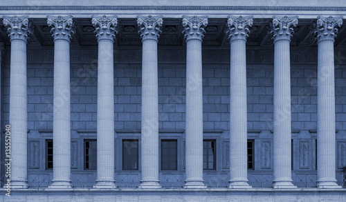 Corinthian columns in a colonnade of a building facade. The neoclassical style resembles a law court / courthouse, university, library or public administration building. Blue color tone.