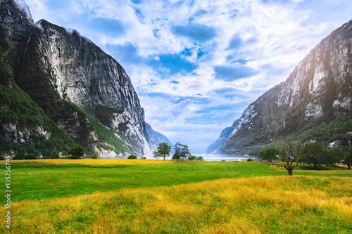 Sunny day scenery by Lysefjord valley, green meadow in canyon between rocks. Lysefjord is popular travel destination for wanderers. Wild nature of Norway, Scandinavia.