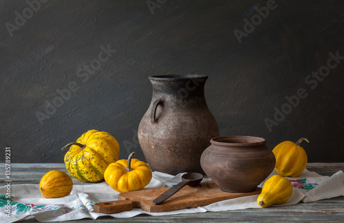 Still life in a rustic style: autumn harvest: wicker basket, pumpkins and wooden spoon on a table. Natural light from a window.