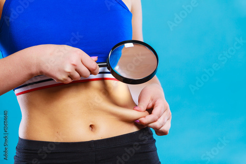 Woman pinches her waist examining it with magnifying glass